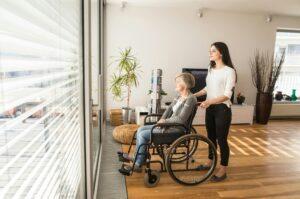 elderly woman sitting in wheelchair being aided by a younger woman