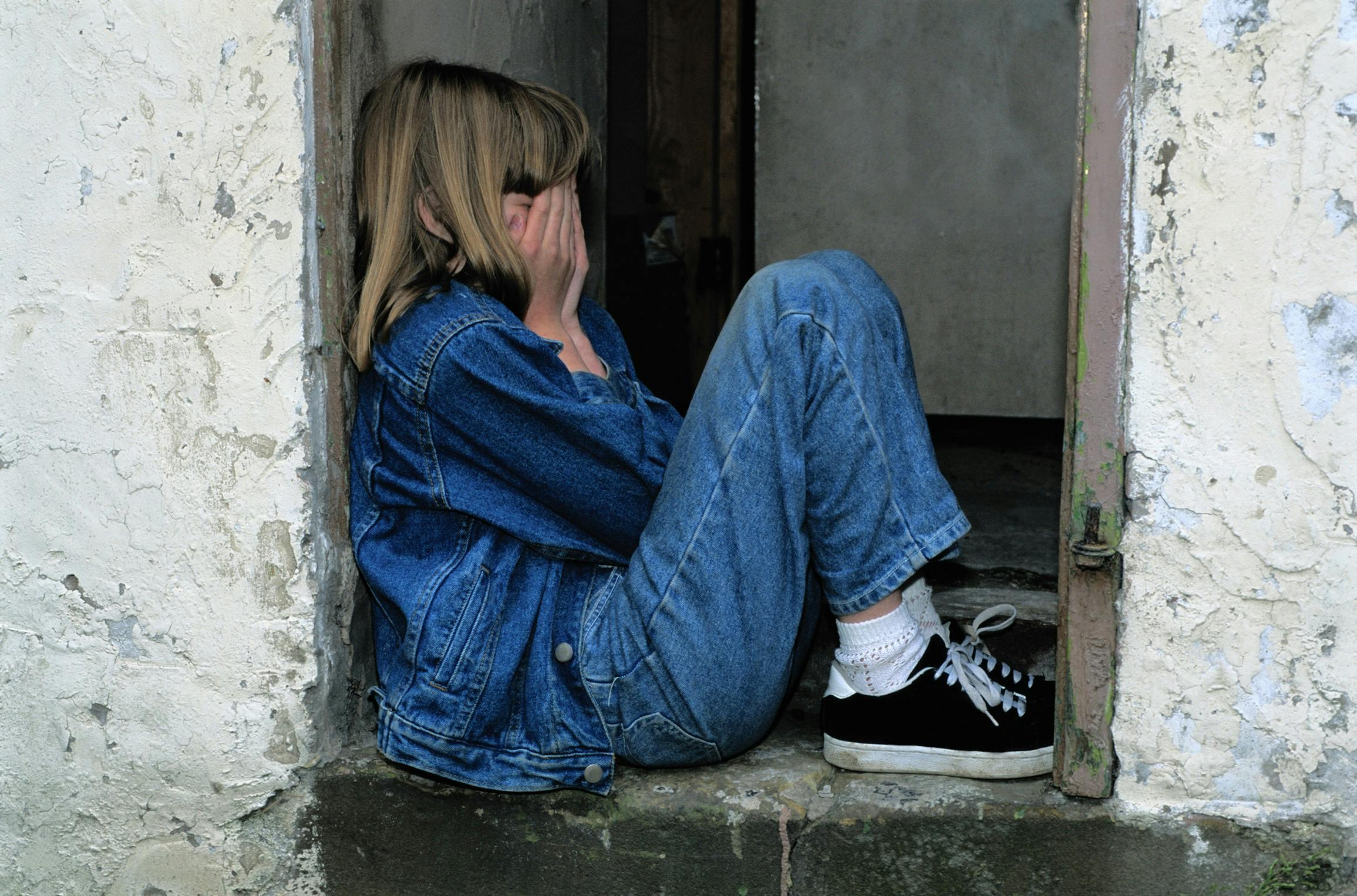 Photo of crying child sitting against a wall