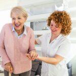 A woman assists an older woman using a walker, providing support and guidance in a caring manner.