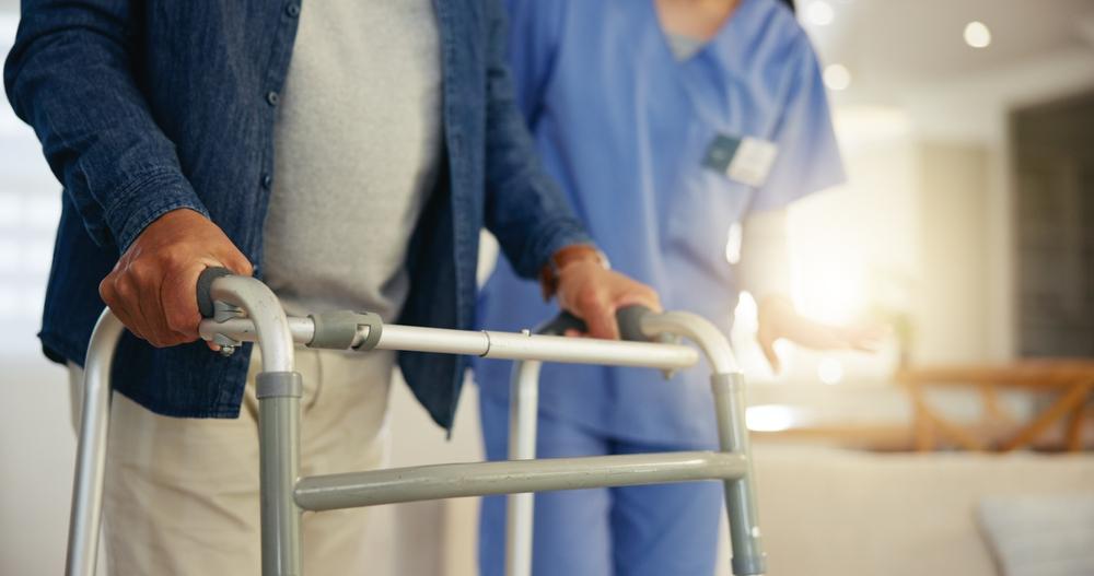 Nurse in scrubs assisting an older person using a walker