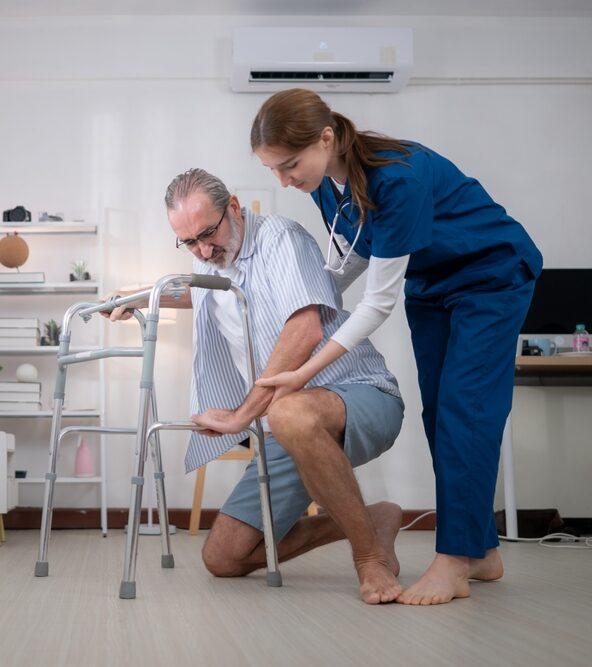 Woman in medical scrubs helping an elderly man use a walker to get up from the floor